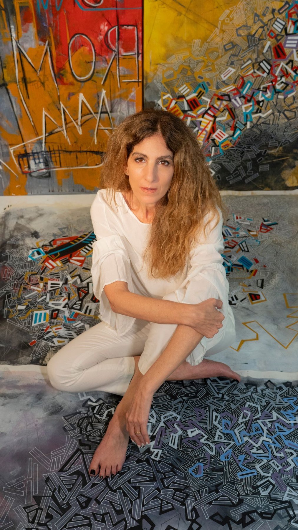 Paola Lettieri seated among her paintings in the studio.